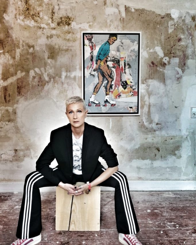 Person in modern Kleidung sitzt auf einem Holzkasten vor einem bunten Wandbild.